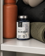 Bote de Fat Burner de Natnatura en una estantería, junto a una botella y una toalla